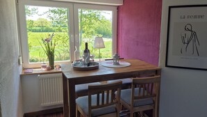 Ein Essbereich mit Tisch für zwei Personen, einem Fenster mit Blick auf Grünflächen und einem gerahmten Kunstwerk an der Wand.