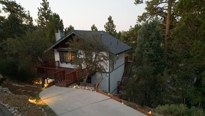 A cabin with a wooden deck, a stone pathway, and a forested backdrop.