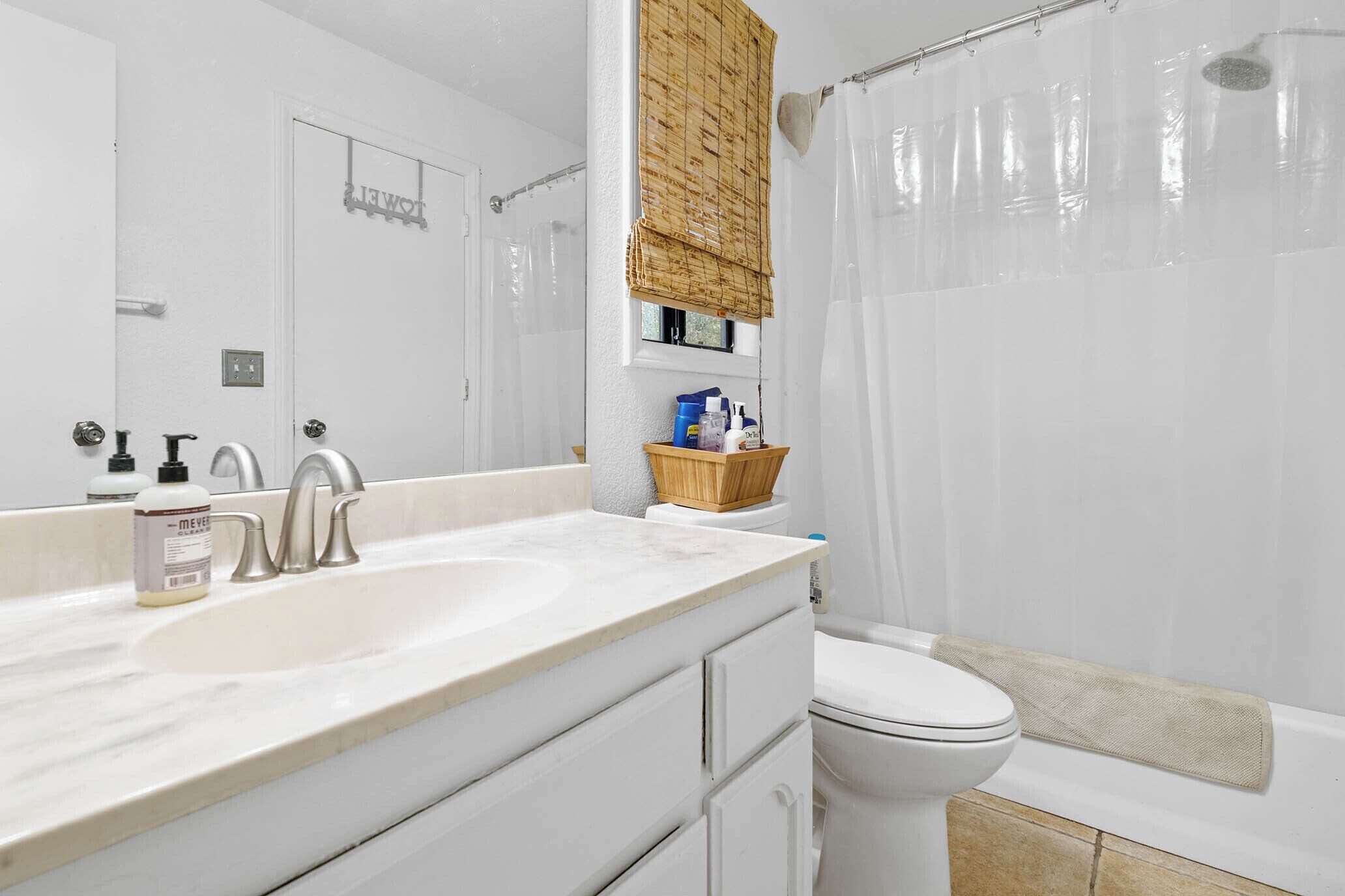 Une salle de bain avec un lavabo blanc, un miroir, des toilettes et un rideau de douche.