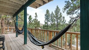 A wooden deck with a hammock, wooden railings, and a view of pine trees.