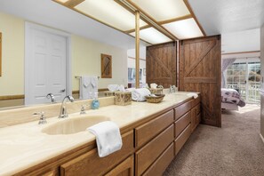 A bathroom with a double sink, wooden cabinets, a large mirror, and a view of a balcony. - Moonridge Golf Escape (Big Bear Lake)