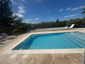 A rectangular swimming pool with a tiled deck, surrounded by lounge chairs and a wooden deck. - Cozy 2-bedroom house in charming Big Pine Key with canal view and relaxing pool (Big Pine Key)