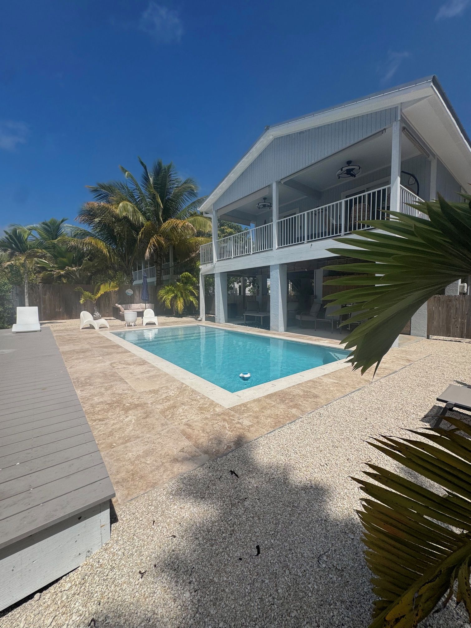 A two-story building with a swimming pool, outdoor seating, and palm trees.