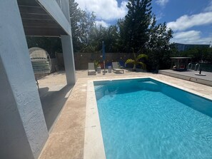 A swimming pool with a wooden deck, lounge chairs, and a small palm tree.