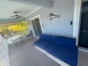 A covered outdoor area with a blue sofa, a table with chairs, and a ceiling fan. - Cozy 2-bedroom house in charming Big Pine Key with canal view and relaxing pool (Big Pine Key)
