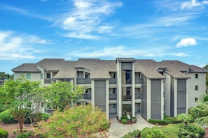 A multi-story residential building with a grey exterior, balconies, and a landscaped garden area.