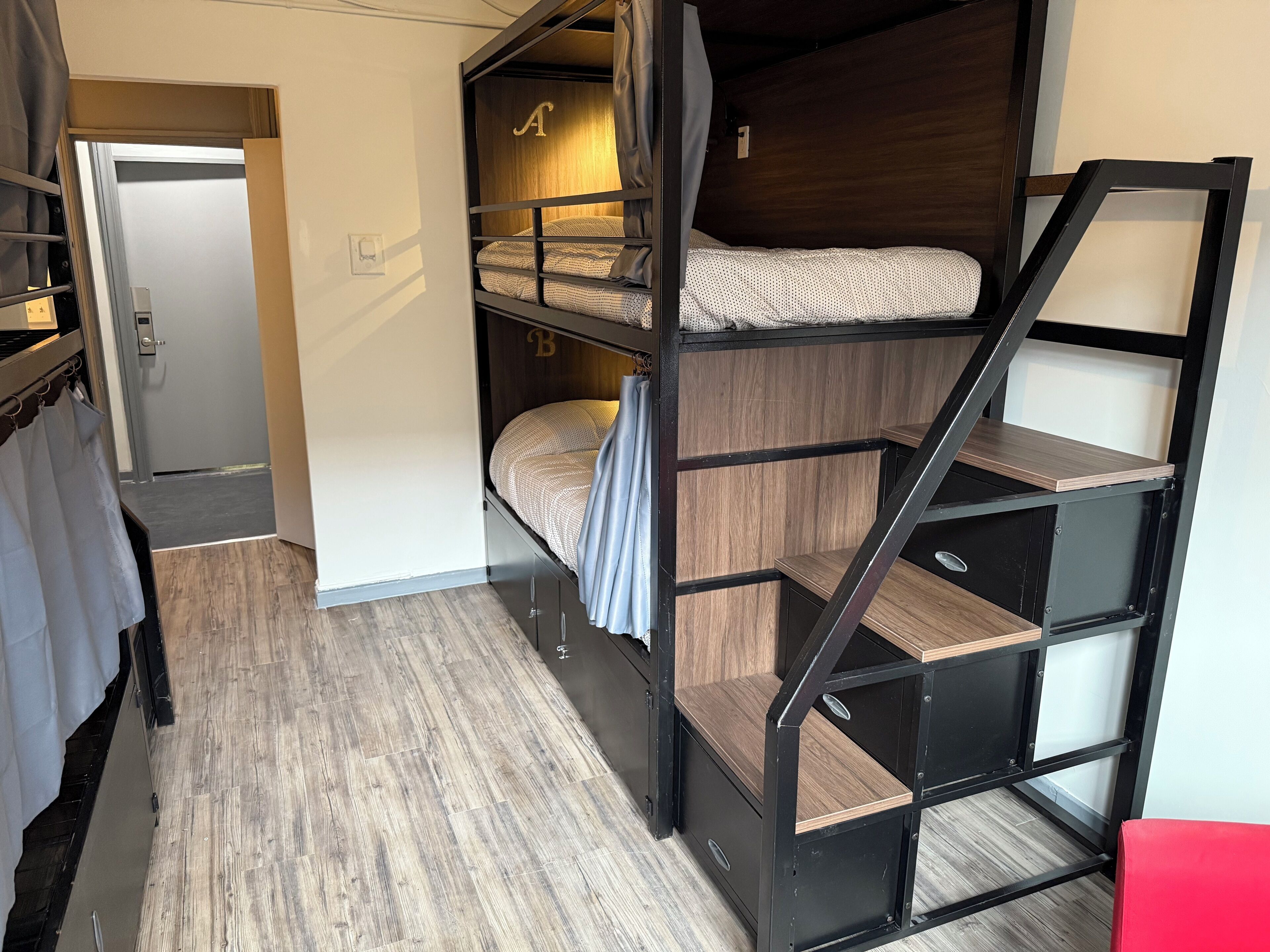 A bunk bed room with a wooden floor, a door, and a red chair.