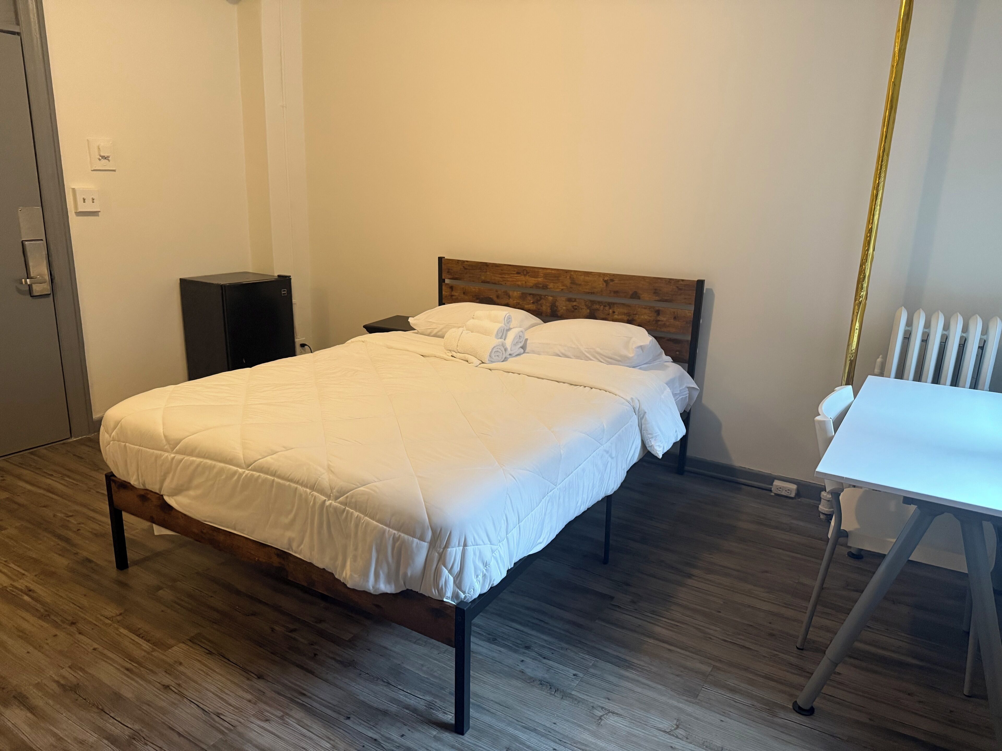 A neatly made bed with white bedding, a wooden headboard, and a white table to the right.