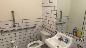 A bathroom with white tiled walls, a toilet, a sink with a mirror, and handrails.