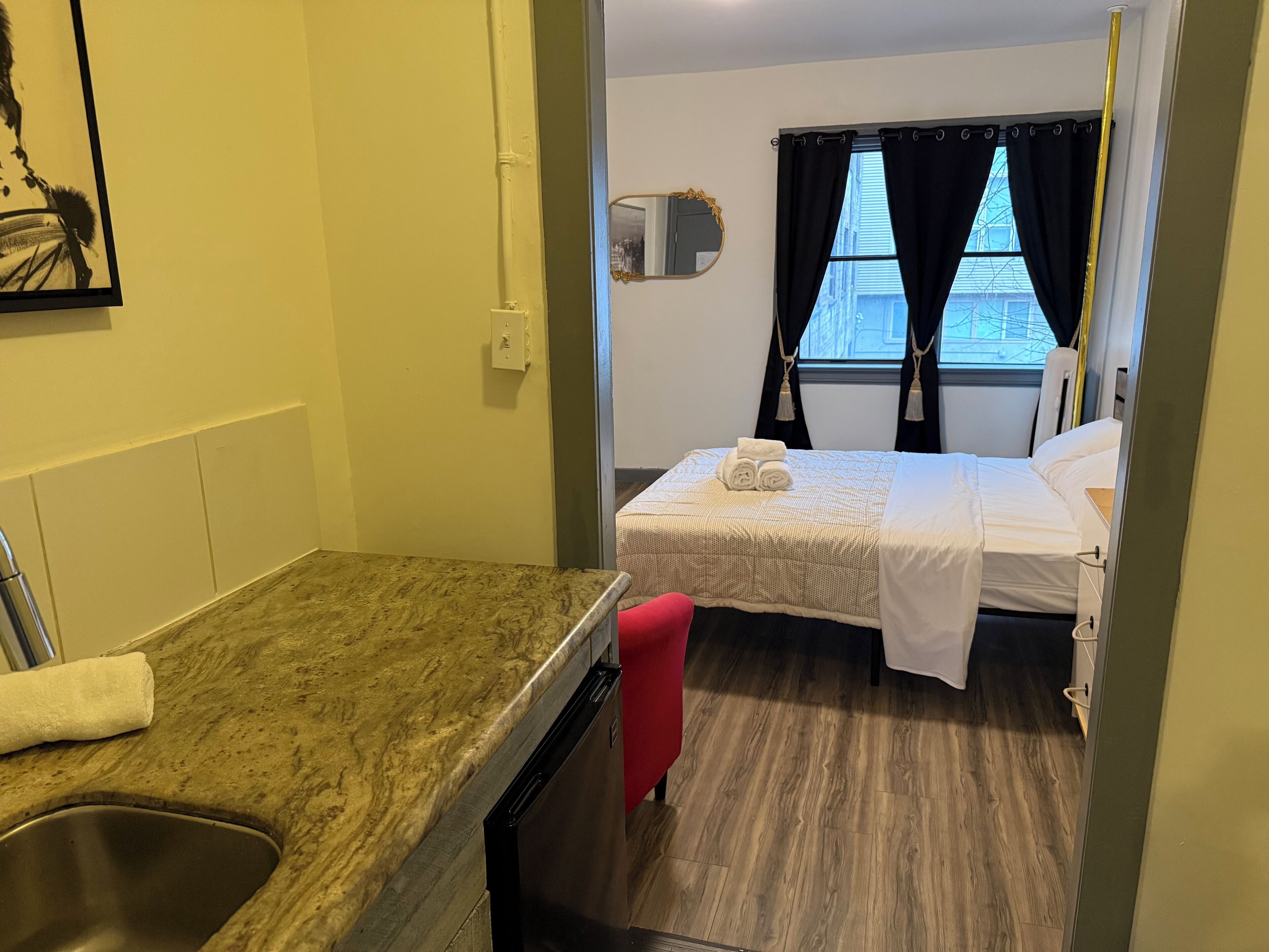 Ein kleines, sauberes Zimmer mit einem Bett, einem Waschbecken und einem Fenster mit Vorhängen.