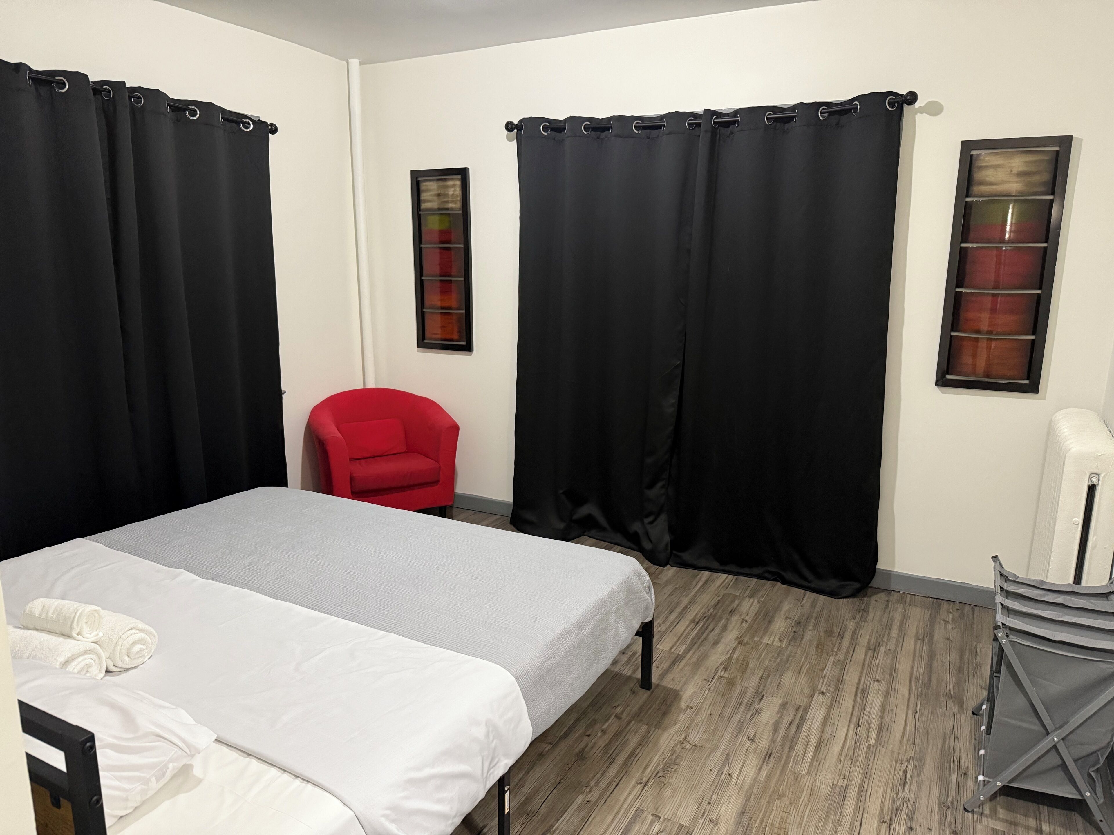 A room with a bed, a red chair, black curtains, and a radiator.