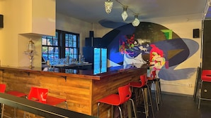 Una zona de bar con mostrador de madera, taburetes rojos y un mural abstracto moderno en la pared.