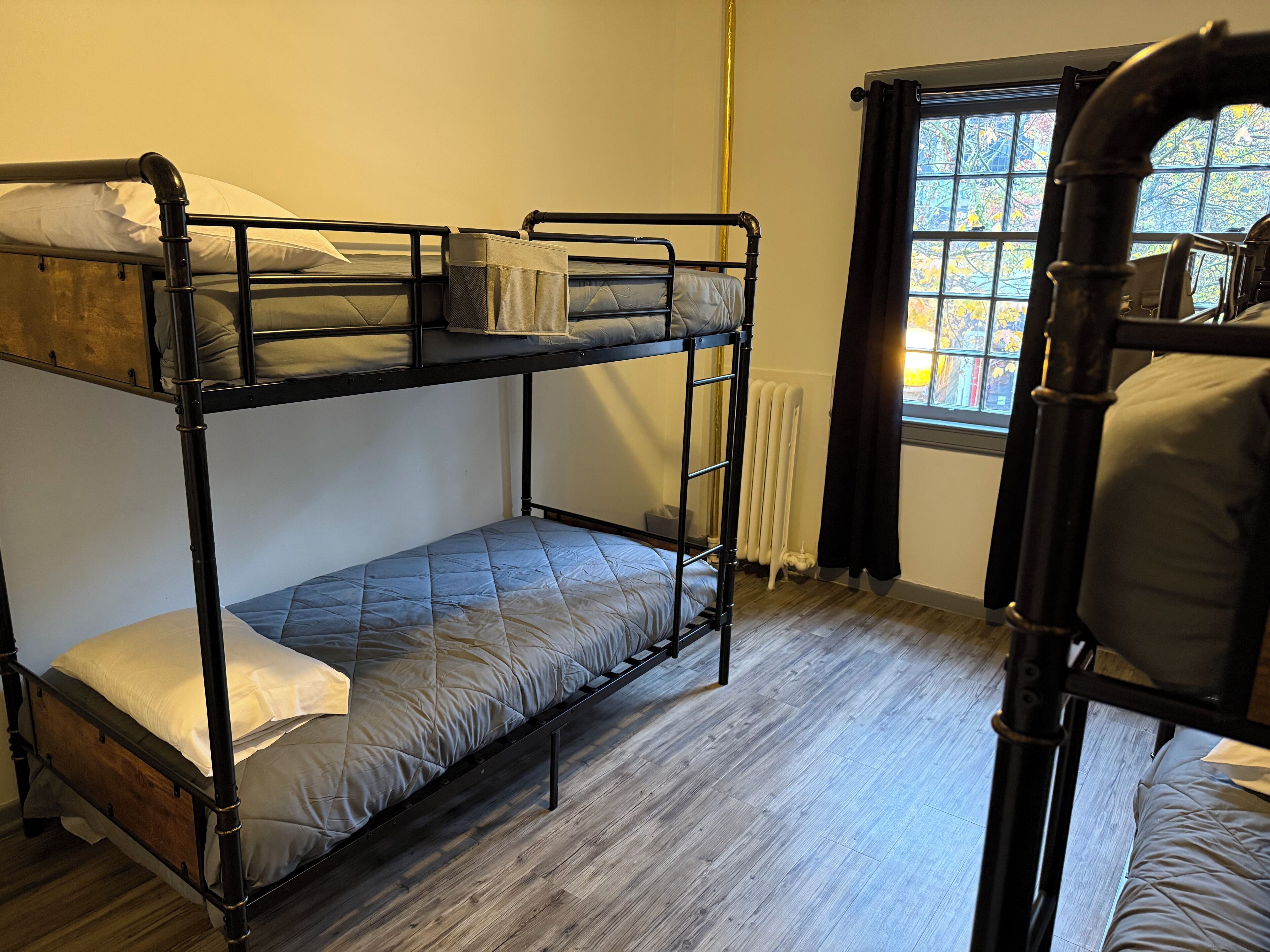 A bunk bed room with a window, wooden flooring, and a radiator.