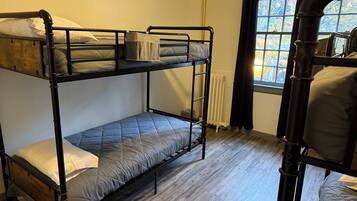 A bunk bed room with a window, wooden flooring, and a radiator.