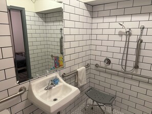 A bathroom with white subway tiles, a white sink with a soap dispenser, a handheld showerhead, a grab bar, and a small step stool. - Hostel Fish Seattle (Seattle)