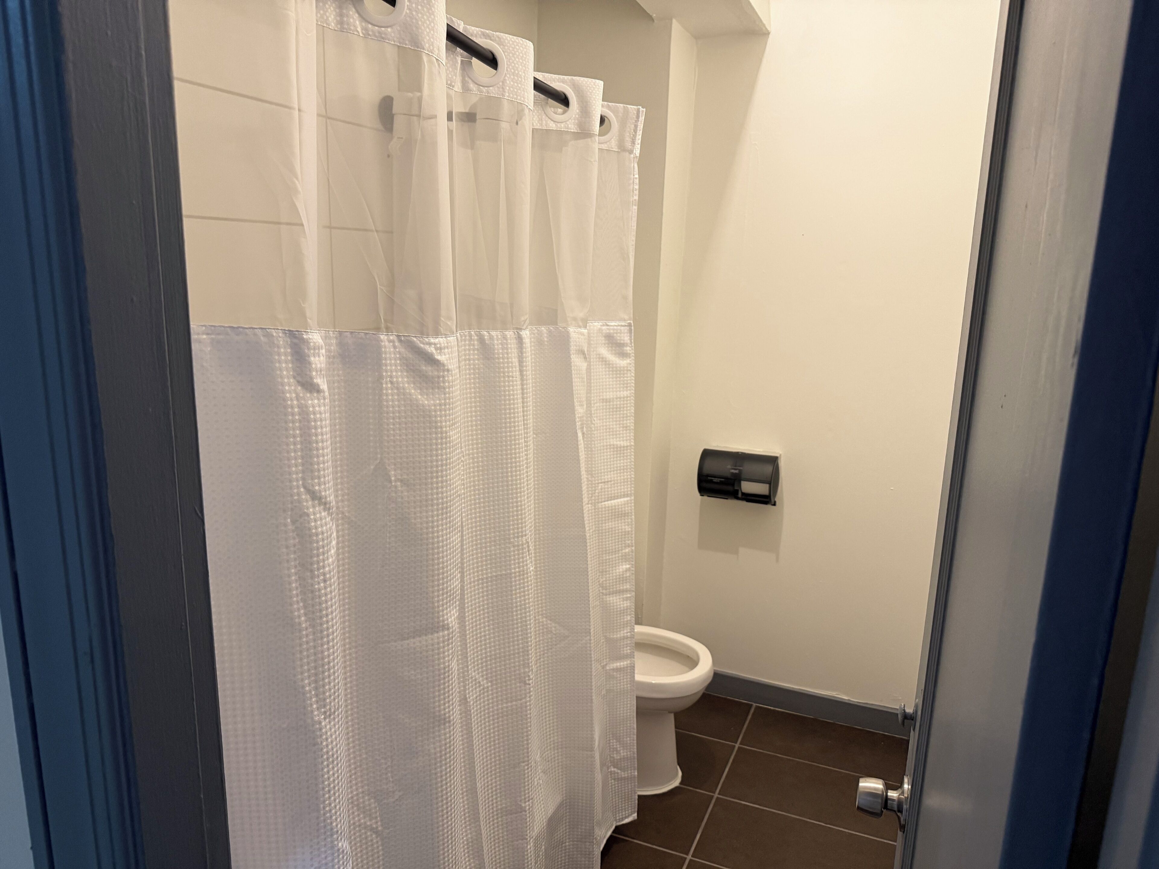 Een badkamer met een toilet, een papieren handdoekdispenser en een douchegordijn.