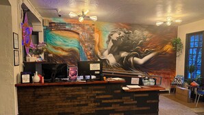 Una recepción con un mural, computadoras y un cartel que indica que no hay huéspedes detrás del mostrador.