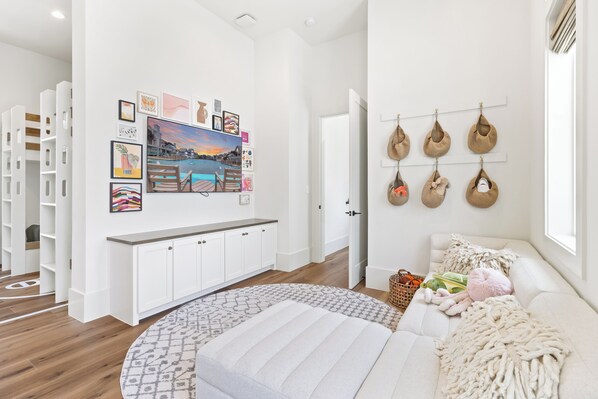 A modern living room with a sofa, a patterned rug, and a wall with framed artwork and hanging bags. - Sage and Sea 112 CRE (Port Aransas)