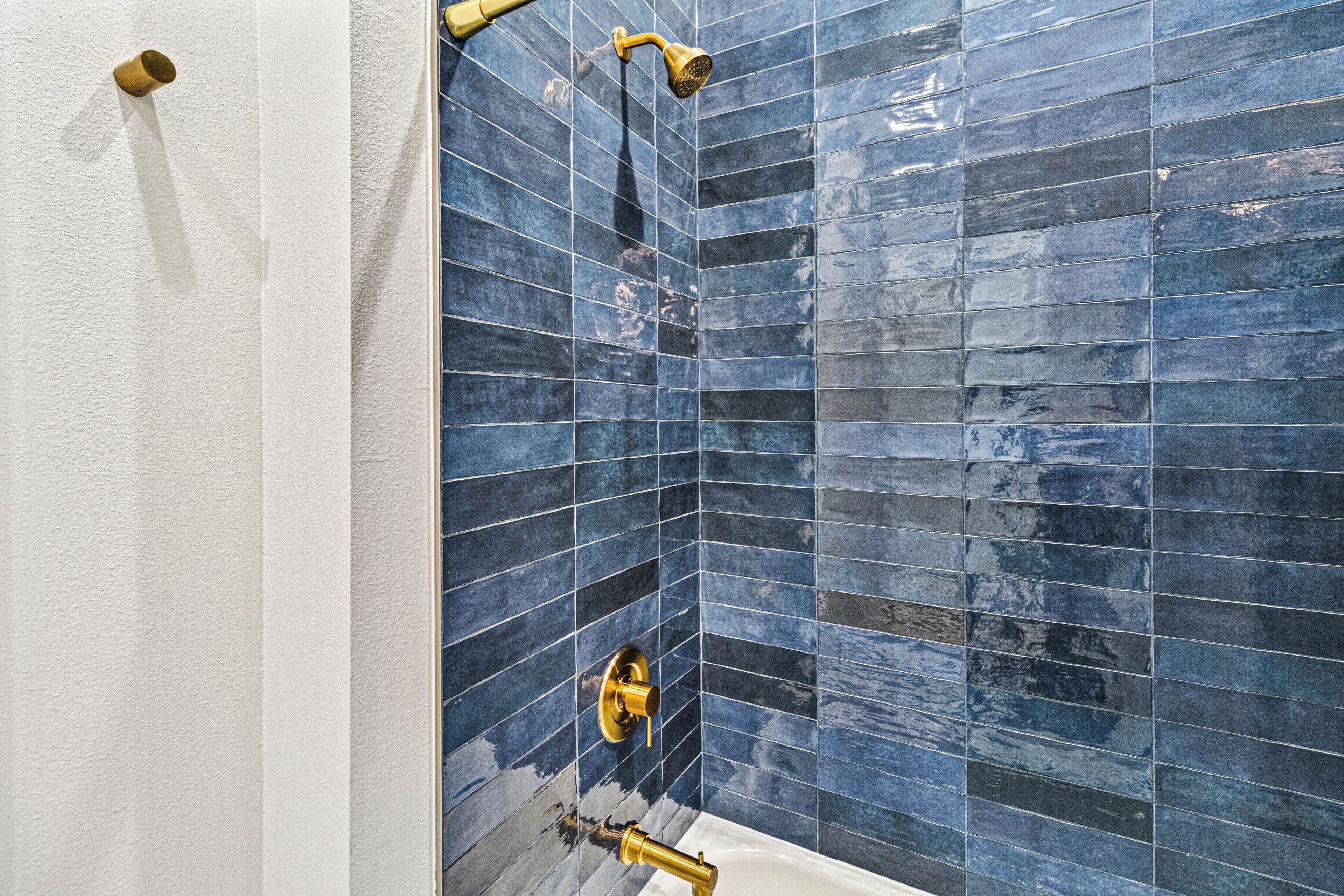 A bathroom with blue-tiled walls, a white bathtub, and gold fixtures.