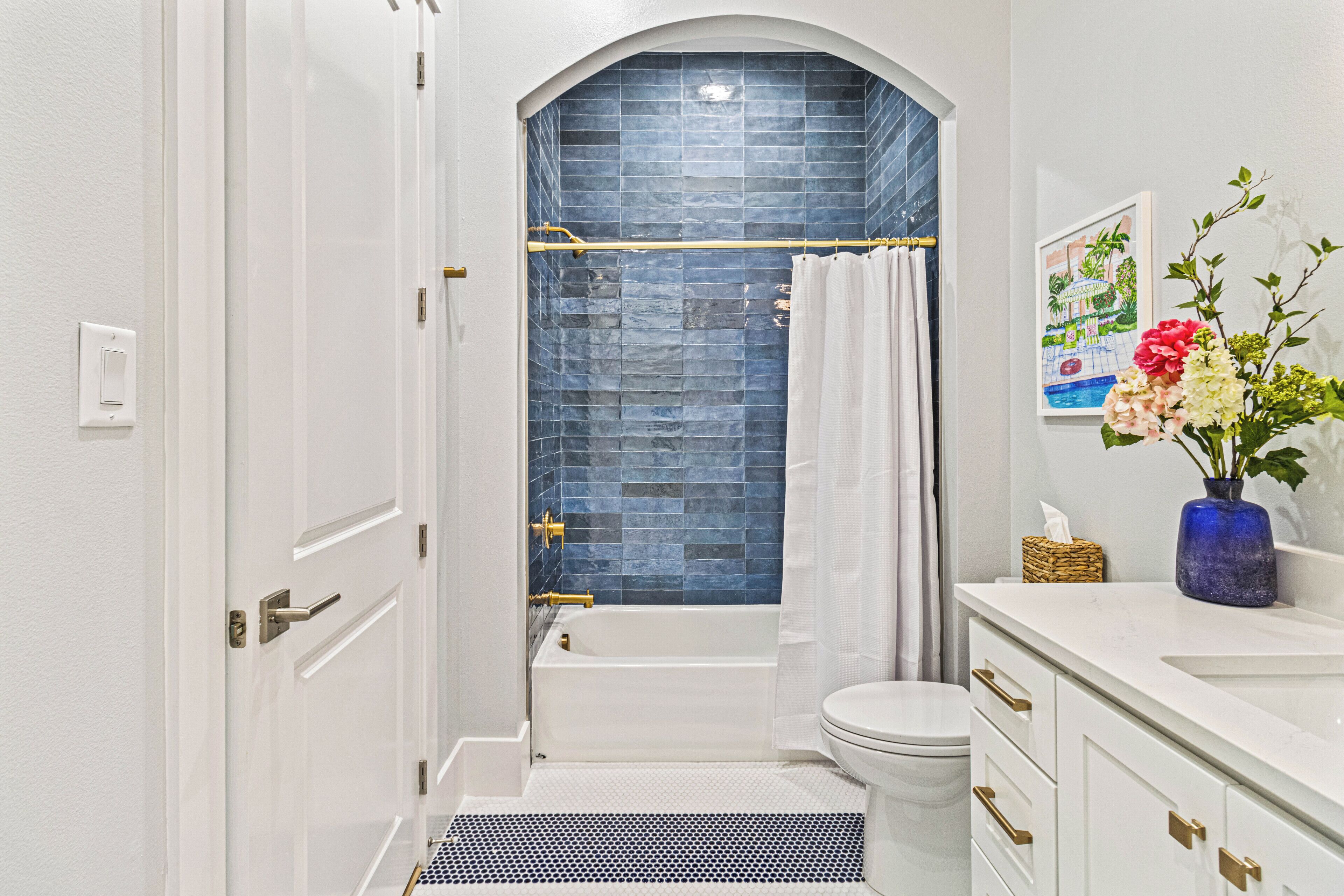 A bathroom with a white bathtub, a white toilet, and a shower area with a blue tiled wall.