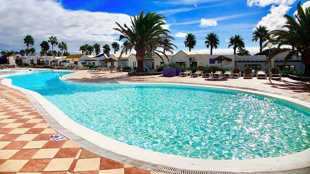 Una piscina con solárium de baldosas, rodeada de palmeras y sillas de descanso.