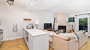 A modern living room with a fireplace, sofa, TV, and kitchen area. - Hank's Lake & Links: The Legend (Biwabik)