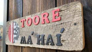 Ein Holzschild mit der Aufschrift 'TOORE MA'HAI' auf einer Holzfläche.
