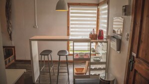 Eine kompakte Küche mit einer zentralen Kochinsel, zwei Barhocker, einer Hängelampe und einem Fenster mit Jalousien.