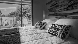 Ein Schlafzimmer mit großem Fenster, einem Bett mit gemusterten Kissen und rustikaler Wanddekoration.