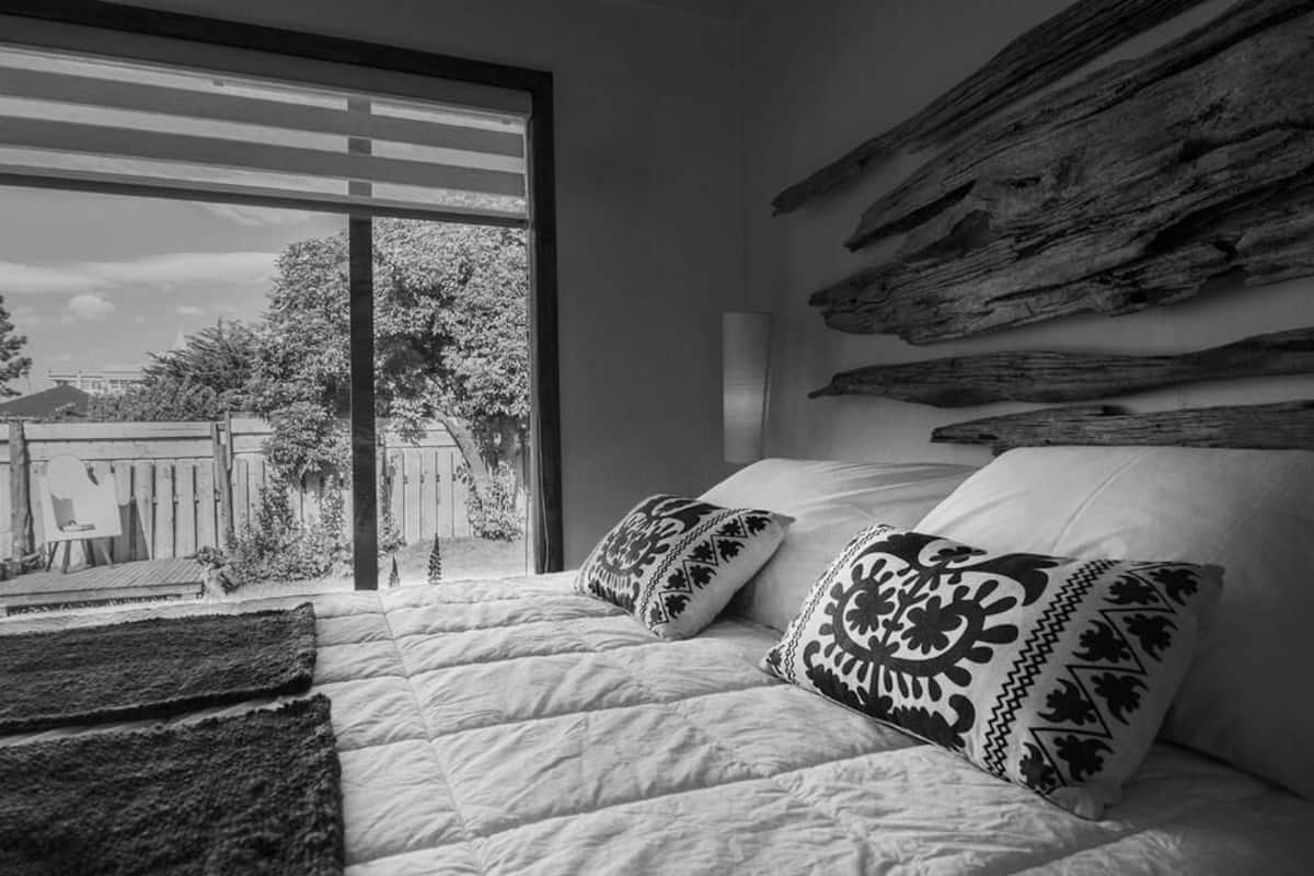 Une chambre dotée d’une grande fenêtre, d’un lit agrémenté d’oreillers à motifs et d’une décoration murale rustique.