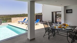 Un área de piscina en la azotea con sillones de descanso, una mesa de comedor lista para el desayuno y una vista despejada del paisaje circundante.