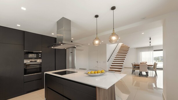 Una cocina moderna con una isla central, electrodomésticos integrados e iluminación colgante.
