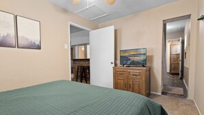 A bedroom with a green bedspread, wooden dresser, and a painting on the wall.