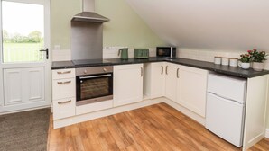 Una cocina con gabinetes blancos, encimera negra, campana de acero inoxidable, microondas, hervidor y refrigerador.