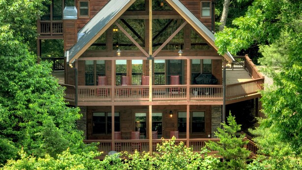 A multi-story cabin with a balcony, surrounded by dense forest.