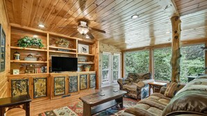 A wooden interior with a television, shelves with decorative items, a sofa, and a patterned rug.