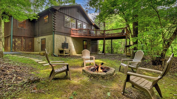 A rustic cabin with a deck, surrounded by lush greenery.