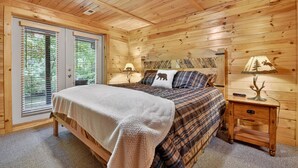 A wooden cabin bedroom with a bed, two bedside tables, and a window with blinds.