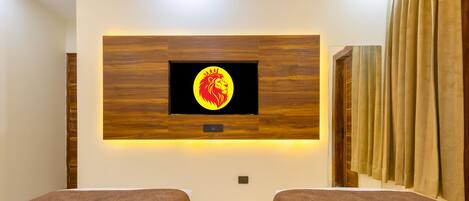 A hotel room with a large wall-mounted TV displaying a lion emblem, two single beds with brown headboards, a marble floor, and a wooden panel wall.