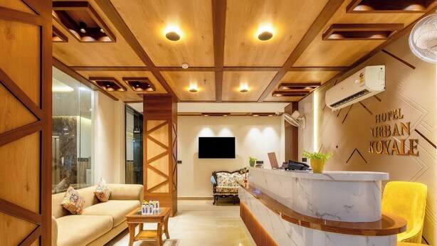 A hotel reception area with a wooden reception desk, a sofa, a small table with items, and a TV mounted on the wall.