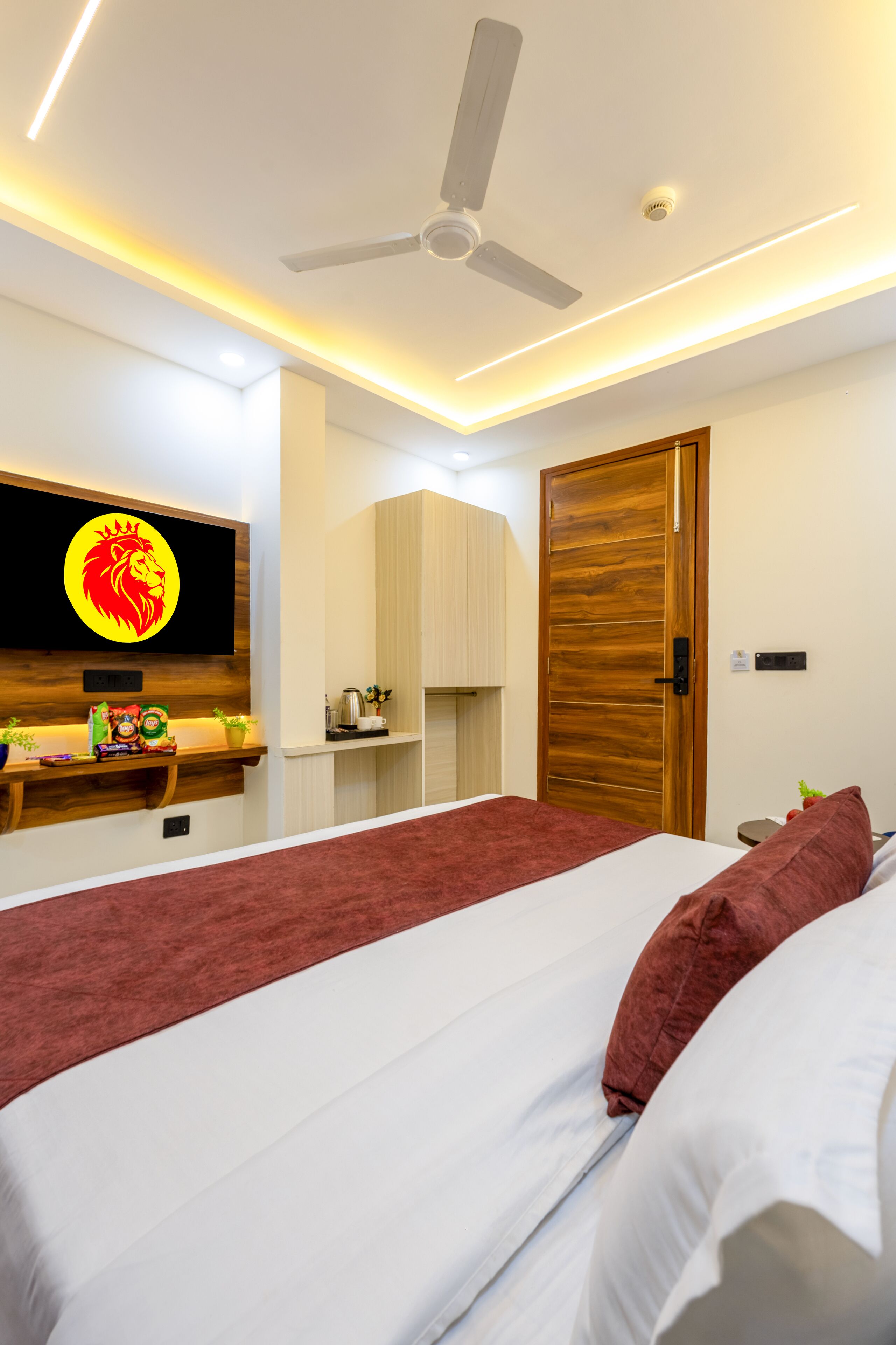 Une chambre à coucher moderne avec un lit, un ventilateur de plafond, un téléviseur fixé au mur et une porte en bois.
