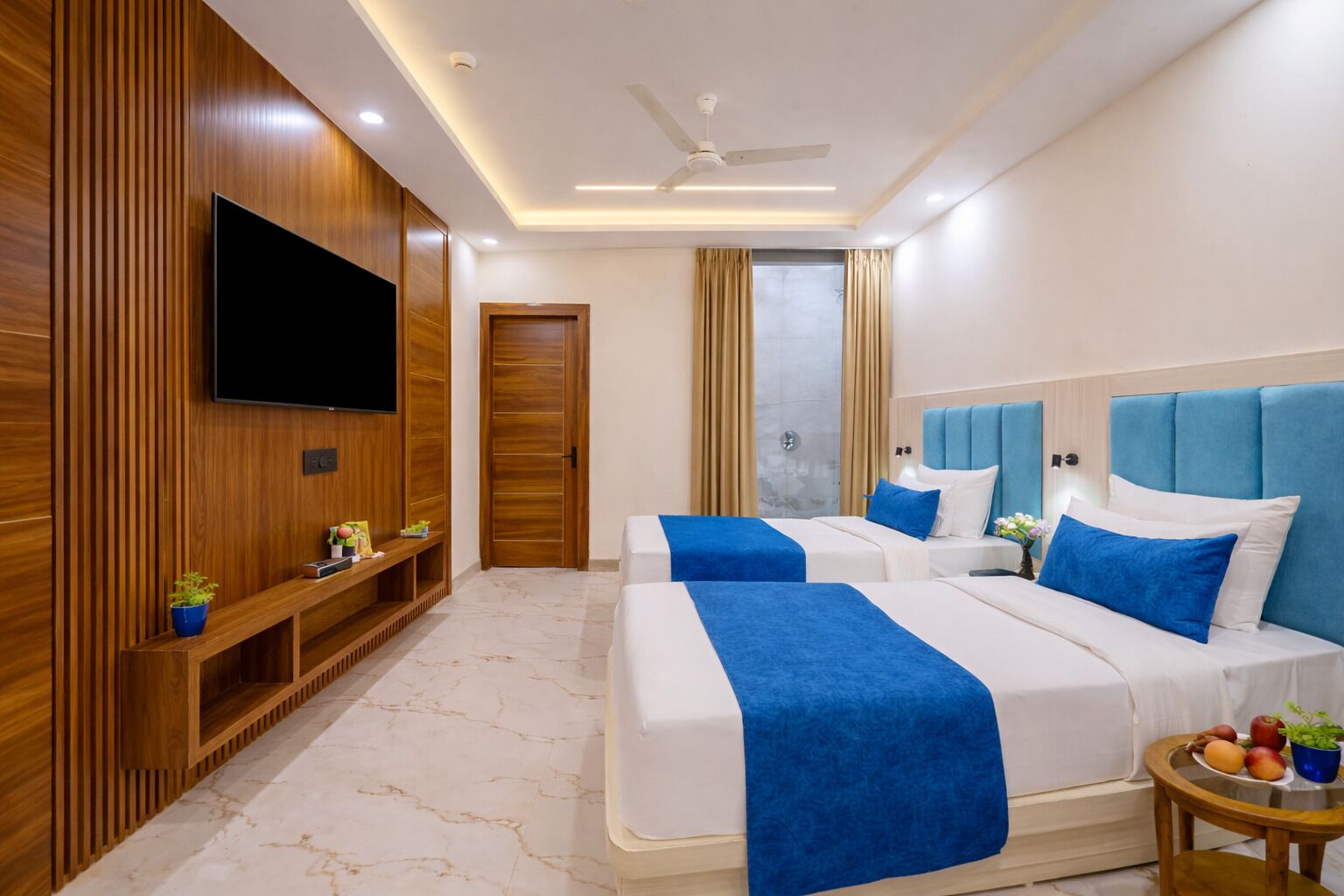 Une chambre d’hôtel avec deux lits, une télévision, un ventilateur de plafond et un sol en marbre.