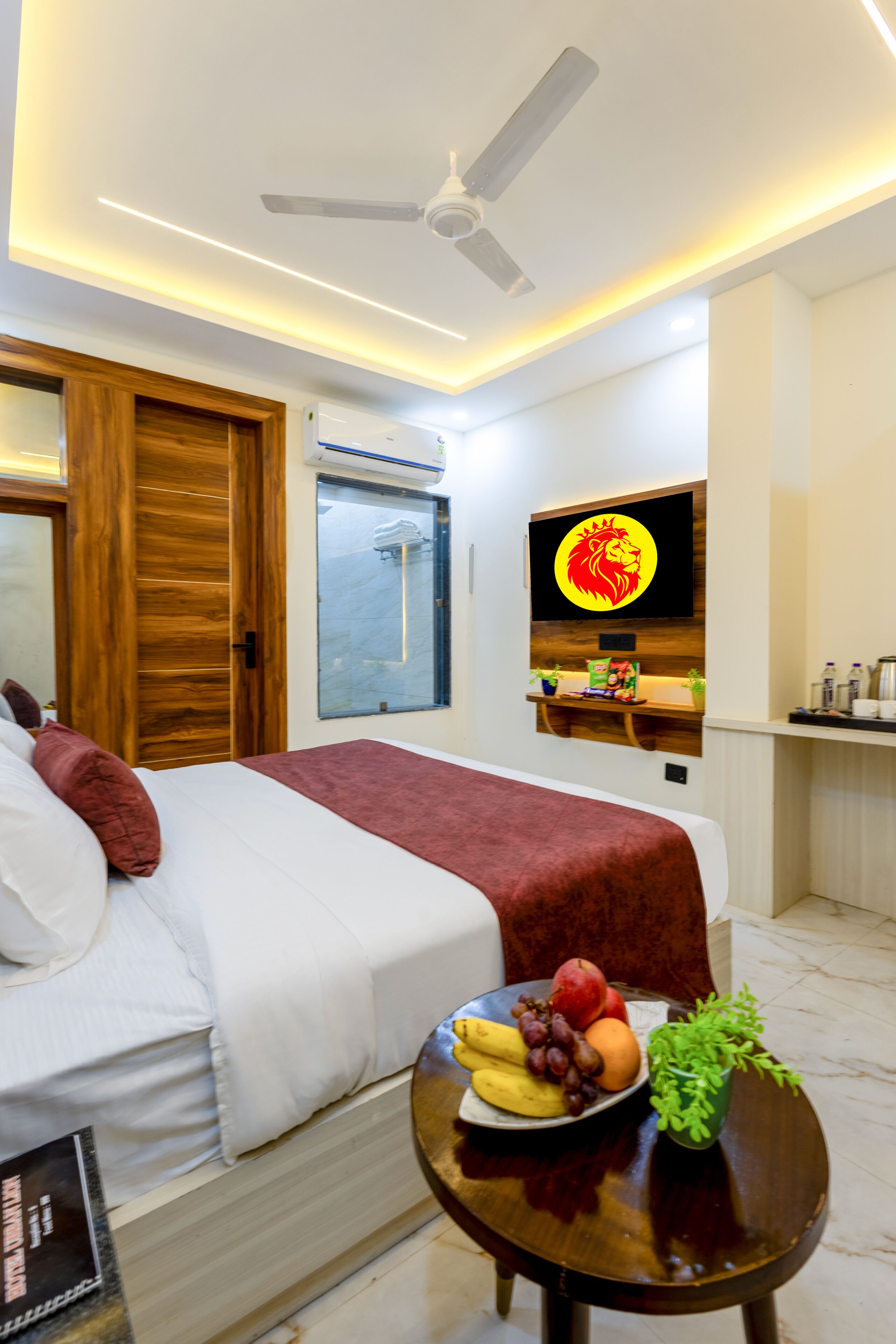 A hotel room with a bed, a TV mounted on the wall, a small table with fruit, and a ceiling fan.