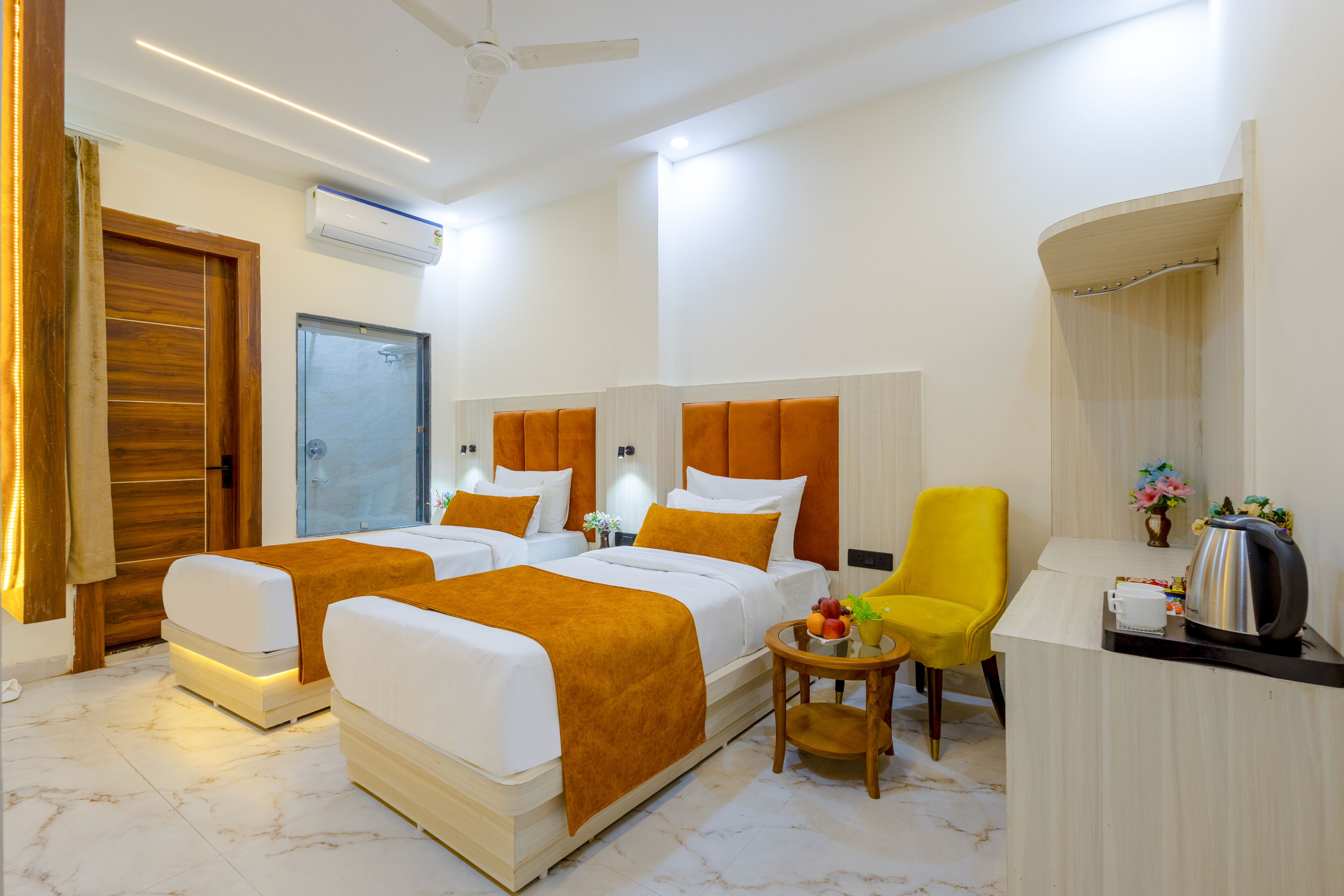 A hotel room with two beds, a desk, a chair, a coffee maker, and a small table with fruit.