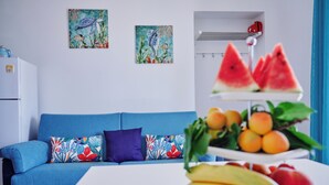 A modern living room with a blue sofa, colorful cushions, two wall art pieces, a white table with fruit, and a white refrigerator. - Cozy waterfront apartment, 10 min.ValledeiTempli-Casa al Mare Circe (San Leone)