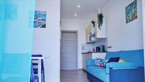 A compact living space with a blue sofa, a small dining table, and a kitchenette. - Cozy waterfront apartment, 10 min.ValledeiTempli-Casa al Mare Circe (San Leone)
