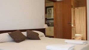 A hotel room with a bed, pillows, a nightstand, a mirror, and a bathroom visible through an open door. - Apart Riviera Tower Suites (Villa Carlos Paz)