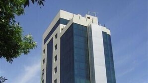 A modern high-rise building with a glass facade, surrounded by trees and a ground-level commercial area with signage. - Apart Riviera Tower Suites (Villa Carlos Paz)