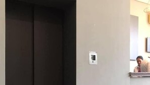 Un couloir avec un ascenseur fermé et un interphone fixé au mur.