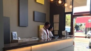 Un comptoir d’accueil avec deux employés, un intérieur moderne agrémenté de luminaires suspendus et des certificats encadrés accrochés au mur.